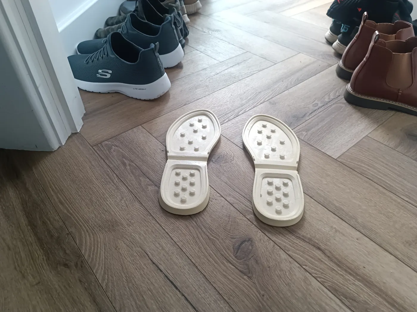 Two white soles left on a herringbone hallway floor, uppers gone inside.